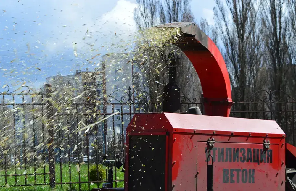 Из измельчителя веток летят щепки